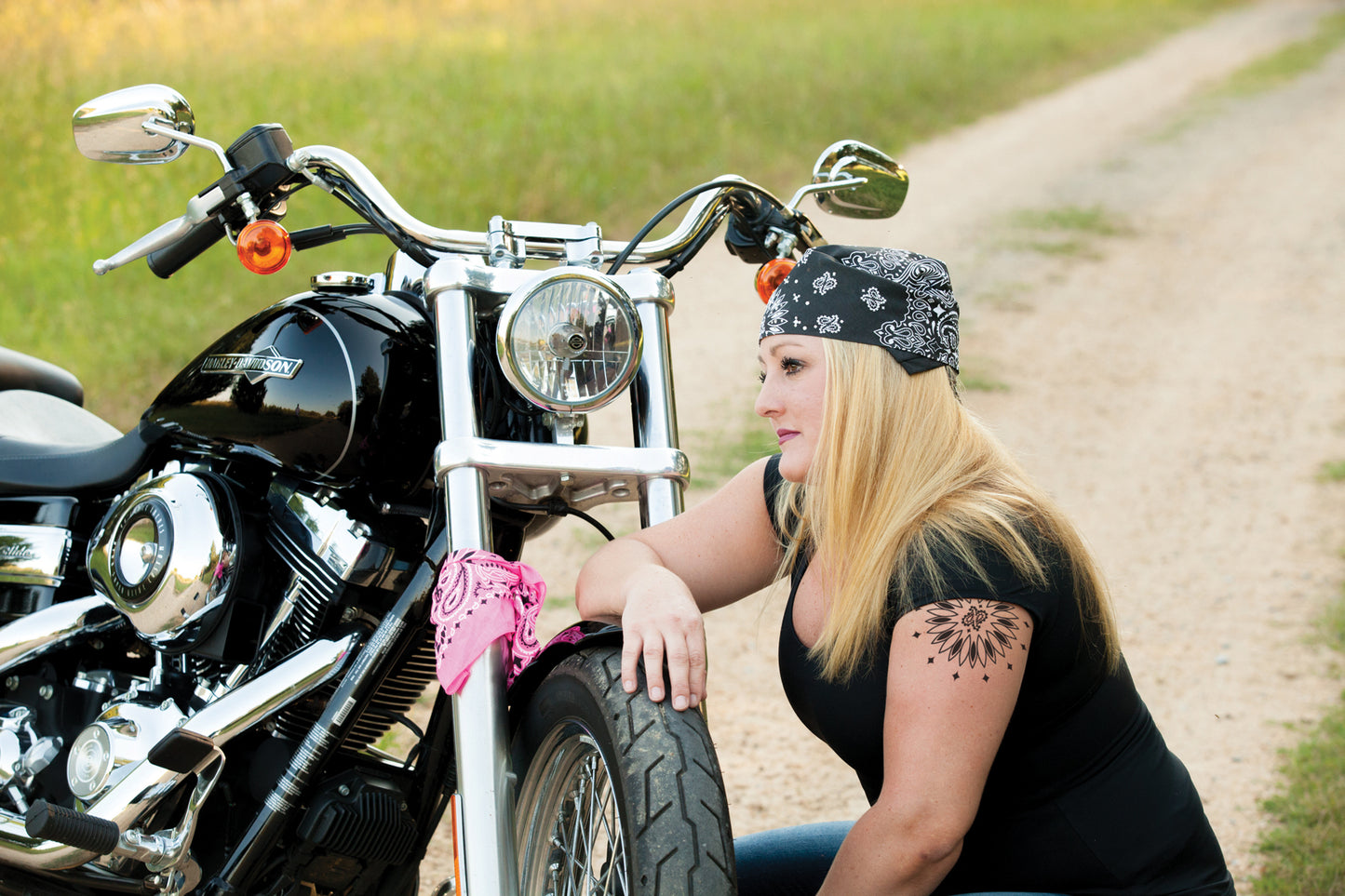 Woman with motorcycle wearing 12-Pack USA Made Paisley Bandanna - BLACK in traditional design, sitting on a rural road.